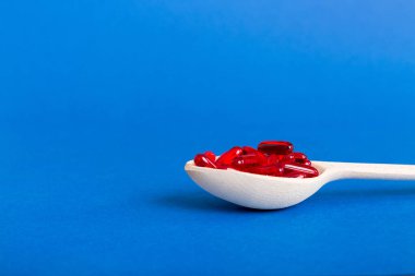 Renkli bir arka planda kaşıkta vitamin kapsülleri. Haplar sağlıklı bir yemek olarak sunuldu. Kırmızı yumuşak jel vitamin takviye kapsülleri kaşık üzerinde.
