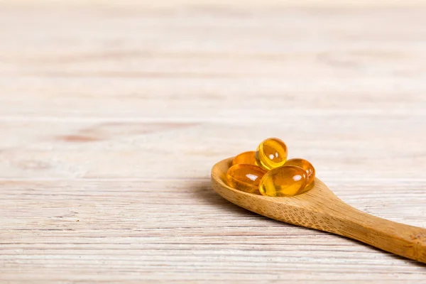 Vitamin omega capsules in a spoon on a colored background. Pills served as a healthy meal. Red soft gel vitamin supplement capsules on spoon.