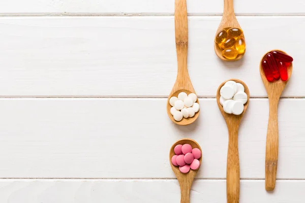 Vitamin capsules in a spoon on a colored background. Pills served as a healthy meal. Red soft gel vitamin supplement capsules on spoon.