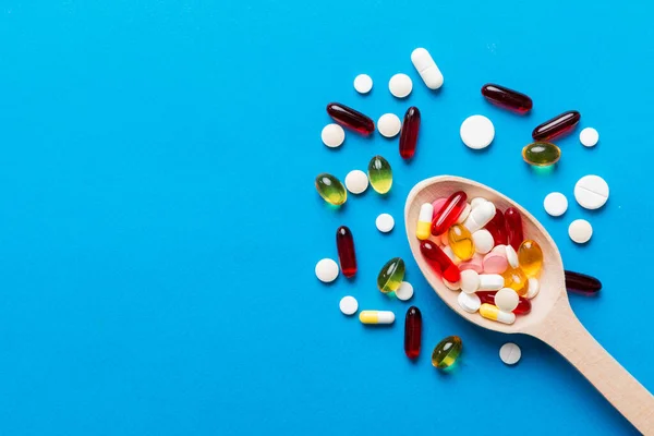 Vitamin capsules in a spoon on a colored background. Pills served as a healthy meal. Red soft gel vitamin supplement capsules on spoon.