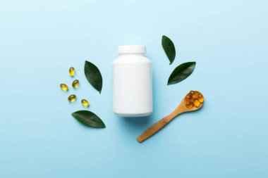 Omega-3 kapsülleri yeşil yapraklı arka planda beyaz bir şişede yatar. Balık yağı tabletleri. Biyolojik olarak aktif katkı maddeleri. Omega 6, Omega 9, A vitamini, E, D vitamini, D3 vitamini..