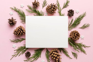 Noel kompozisyonu düzdü. Kare kağıt boş, çam ağacı dalları, renkli arka planda noel süslemeleri. Üst görünüm, metin için boşluk kopyala.