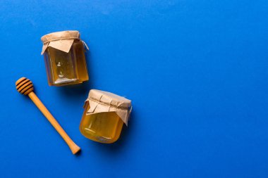 Renkli arka planda tahta çiselemeli cam bal kavanozu. Bal küpü ve dipper yükseklerde. Üst görünüm kopyalama alanı.
