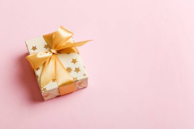 Noel 'i ya da diğer tatil hediyelerini renkli arka planda altın kurdeleli beyaz kağıda sardım. Şimdiki kutu, renkli tabloda hediye süslemesi, kopya alanı ile üst görünüm.