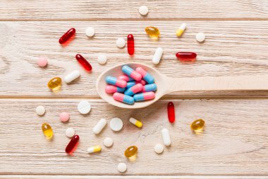 Renkli bir arka planda kaşıkta vitamin kapsülleri. Haplar sağlıklı bir yemek olarak sunuldu. Kırmızı yumuşak jel vitamin takviye kapsülleri kaşık üzerinde.