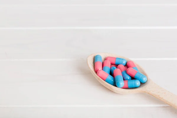 Vitamin capsules in a spoon on a colored background. Pills served as a healthy meal. Red soft gel vitamin supplement capsules on spoon.