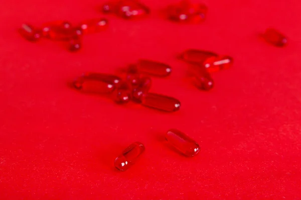 Heap of red pills on colored background. Tablets scattered on a table. Pile of red soft gelatin capsule. Vitamins and dietary supplements concept.