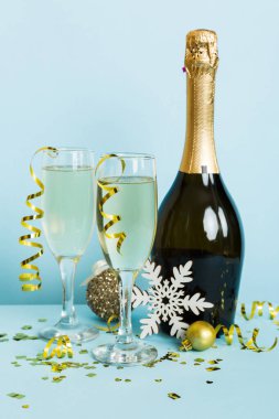 Champagne bottle with confetti, glasses and christmas decor on colored holiday background. Flat lay New Year decorations.