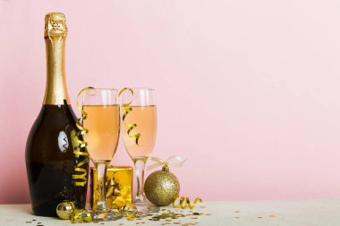Champagne bottle with confetti, glasses and christmas decor on colored holiday background. Flat lay New Year decorations.