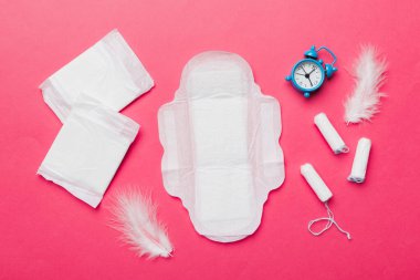 Alarm saatini hijyenik kadın tamponları ve regl pedleri ile çalıyor. Tıbbi konsept kadın kritik günler ve regl dönemi. Kadın günlük hijyen. Boşluğu kopyala.