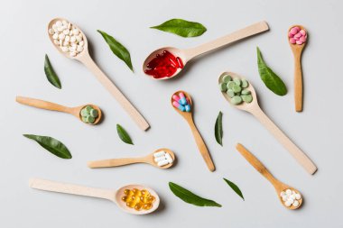 Renkli arka planda tahta kaşıkta vitamin ve mineral haplarının üst görünümü. Muhtelif ilaç haplarının en üst görüntüsü. Beslenme takviyesi sağlık ürünleri.
