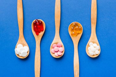 Renkli bir arka planda kaşıkta vitamin kapsülleri. Haplar sağlıklı bir yemek olarak sunuldu. Kırmızı yumuşak jel vitamin takviye kapsülleri kaşık üzerinde.