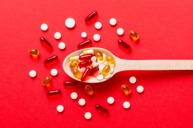 Renkli bir arka planda kaşıkta vitamin kapsülleri. Haplar sağlıklı bir yemek olarak sunuldu. Kırmızı yumuşak jel vitamin takviye kapsülleri kaşık üzerinde.