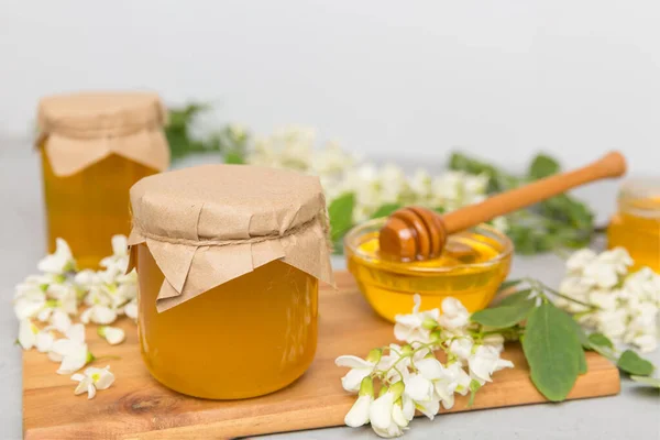 Sweet honey jar surrounded spring acacia blossoms. Honey flows from a spoon in a jar. jars of clear fresh acacia honey on wooden background.