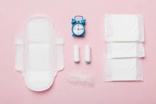 Ringing alarm clock with sanitary female tampons and menstrual sanitary pads. Medical concept of woman critical days and menstruation. Female daily hygiene. Copy space.