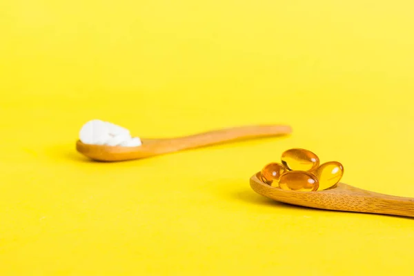 Vitamin capsules in a spoon on a colored background. Pills served as a healthy meal. Red soft gel vitamin supplement capsules on spoon.