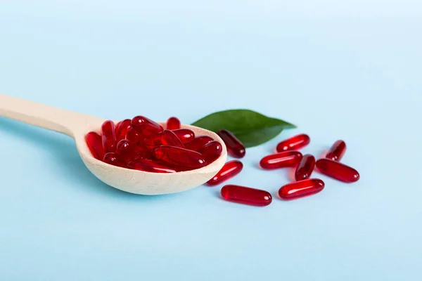 Vitamin capsules in a spoon on a colored background. Pills served as a healthy meal. Red soft gel vitamin supplement capsules on spoon.