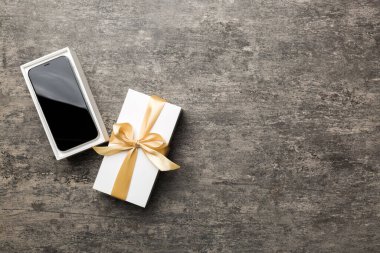 Altın kurdeleli hediye kutusu ve arka planda akıllı telefon, üst manzara. Boş kutu paketleme modeli, tasarımınız için şablon - markalaşma modeli.
