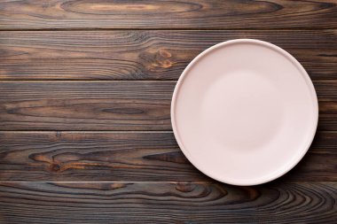 Ahşap arka planda boş pembe tabağın üst görüntüsü. Tasarımın için boş boşluk.