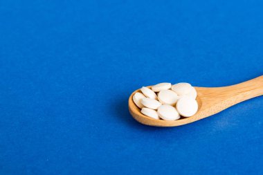 Renkli arka planda bir yığın beyaz hap. Tabletler masaya saçılmış. Kırmızı yumuşak jelatin kapsül yığını. Vitaminler ve beslenme takviyeleri konsepti.