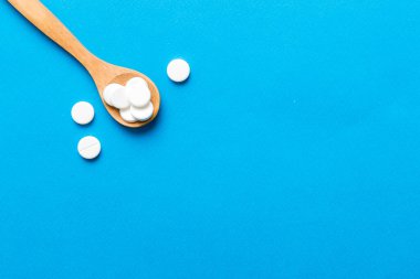 Renkli arka planda bir yığın beyaz hap. Tabletler masaya saçılmış. Kırmızı yumuşak jelatin kapsül yığını. Vitaminler ve beslenme takviyeleri konsepti.