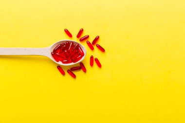 Renkli bir arka planda kaşıkta vitamin kapsülleri. Haplar sağlıklı bir yemek olarak sunuldu. Kırmızı yumuşak jel vitamin takviye kapsülleri kaşık üzerinde.