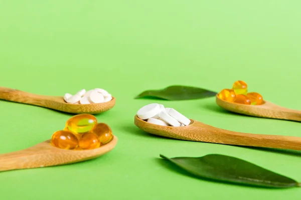 Vitamin capsules in a spoon on a colored background. Pills served as a healthy meal. Red soft gel vitamin supplement capsules on spoon.