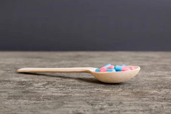 Vitamin capsules in a spoon on a colored background. Pills served as a healthy meal. Red soft gel vitamin supplement capsules on spoon.