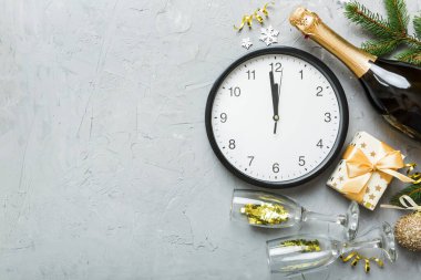 New year celebration concept with a bottle of champagne and two glasses toasting. Christmas gift box, alarm clock and fir tree branch on colored table. Top view Copy space.