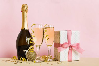 Champagne bottle with confetti, glasses and christmas decor on colored holiday background. Flat lay New Year decorations.