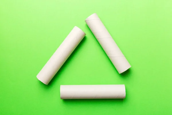 Empty toilet paper roll on colored background. Recyclable paper tube with metal plug end made of kraft paper or cardboard in the form of a recycling sign.