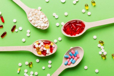 Renkli bir arka planda kaşıkta vitamin kapsülleri. Haplar sağlıklı bir yemek olarak sunuldu. Kırmızı yumuşak jel vitamin takviye kapsülleri kaşık üzerinde.