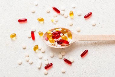 Renkli bir arka planda kaşıkta vitamin kapsülleri. Haplar sağlıklı bir yemek olarak sunuldu. Kırmızı yumuşak jel vitamin takviye kapsülleri kaşık üzerinde.