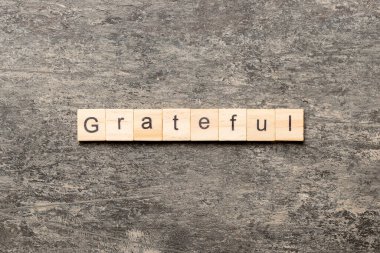 Minnettar kelime ahşap blok üzerinde yazılı. Tablo, minnettar metin kavramı.