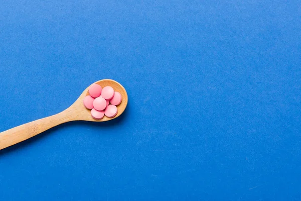 Vitamin capsules in a spoon on a colored background. Pills served as a healthy meal. Red soft gel vitamin supplement capsules on spoon.