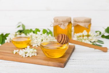 Tatlı bal kavanozu bahar akasyası çiçeklerini sarmıştı. Kavanozdaki kaşıktan bal akar. Tahta zemin üzerinde taze akasya balı kavanozları.