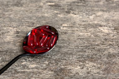 Renkli bir arka planda kaşıkta vitamin kapsülleri. Haplar sağlıklı bir yemek olarak sunuldu. Kırmızı yumuşak jel vitamin takviye kapsülleri kaşık üzerinde.