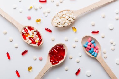 Renkli bir arka planda kaşıkta vitamin kapsülleri. Haplar sağlıklı bir yemek olarak sunuldu. Kırmızı yumuşak jel vitamin takviye kapsülleri kaşık üzerinde.