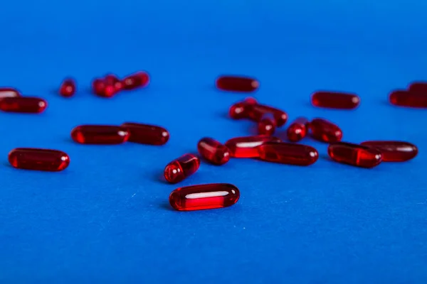 Heap of red pills on colored background. Tablets scattered on a table. Pile of red soft gelatin capsule. Vitamins and dietary supplements concept.