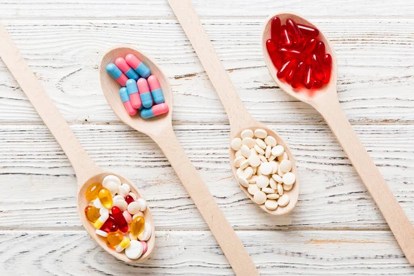 Vitamin capsules in a spoon on a colored background. Pills served as a healthy meal. Red soft gel vitamin supplement capsules on spoon.