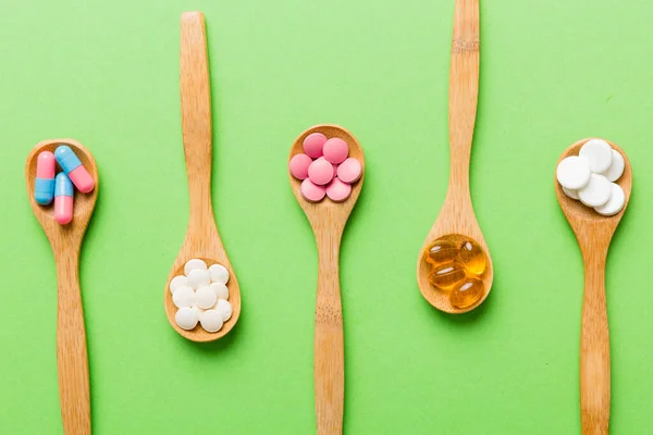 Vitamin capsules in a spoon on a colored background. Pills served as a healthy meal. Red soft gel vitamin supplement capsules on spoon.