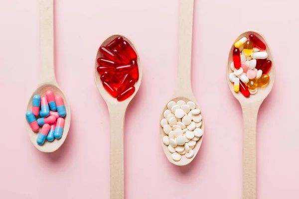 Vitamin capsules in a spoon on a colored background. Pills served as a healthy meal. Red soft gel vitamin supplement capsules on spoon.