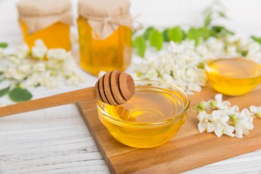 Tatlı bal kavanozu bahar akasyası çiçeklerini sarmıştı. Kavanozdaki kaşıktan bal akar. Tahta zemin üzerinde taze akasya balı kavanozları.