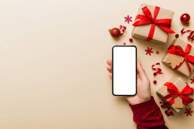 Mesaj atmak için yeri olan bir Noel modeli. Noel reklamı, uygulama şablonu. Masa arkasında boş ekran olan el ele tutuşan telefon. Mutlu yıllar ve Xmas Flat.