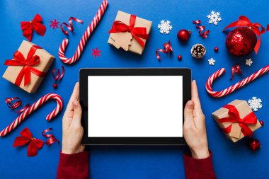 Evden Noel alışverişi, kadın elleri boş beyaz ekranlı tableti tutuyor. Kadın elinde tablet, boş ekran, Noel ağacı ve arka planda hediyeler..