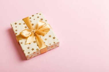 Noel 'i ya da diğer tatil hediyelerini renkli arka planda altın kurdeleli beyaz kağıda sardım. Şimdiki kutu, renkli tabloda hediye süslemesi, kopya alanı ile üst görünüm.