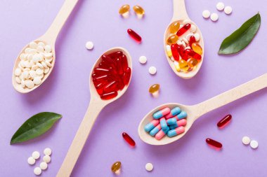 Renkli bir arka planda kaşıkta vitamin kapsülleri. Haplar sağlıklı bir yemek olarak sunuldu. Kırmızı yumuşak jel vitamin takviye kapsülleri kaşık üzerinde.