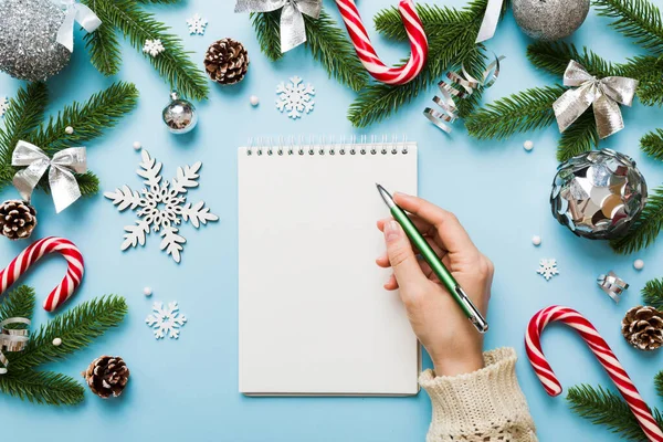 Noel 'i yazmak için bir kadın not defterine Xmas dekorasyonlu renkli arkaplan çiziyor.