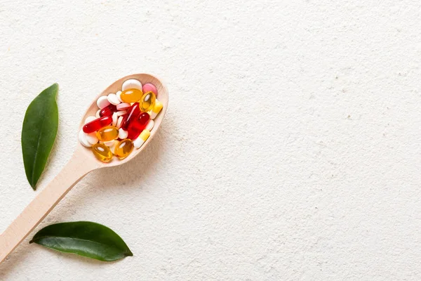 Vitamin capsules in a spoon on a colored background. Pills served as a healthy meal. Red soft gel vitamin supplement capsules on spoon.