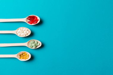 Renkli arka planda tahta kaşıkta vitamin ve mineral haplarının üst görünümü. Muhtelif ilaç haplarının en üst görüntüsü. Beslenme takviyesi sağlık ürünleri.